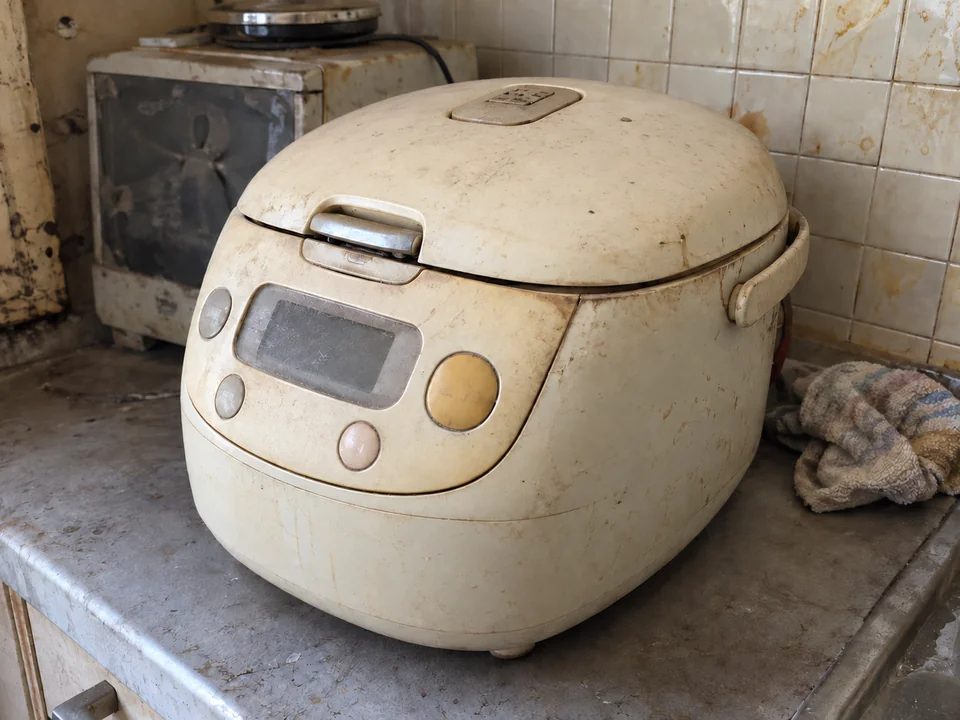 付属品を添えずに置かれた、黄ばみと細かな傷が残る古い炊飯器の本体